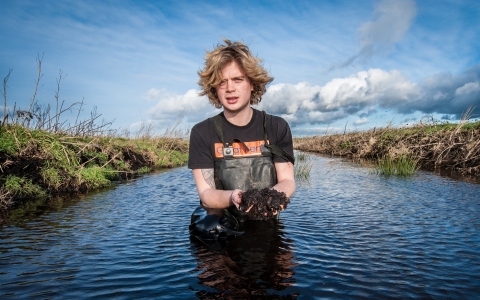 Filip stands in the water holding mud