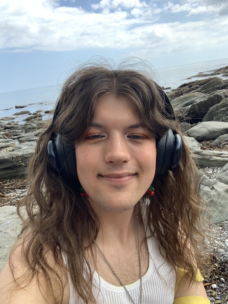 Young person wearing headphones stood on a beach