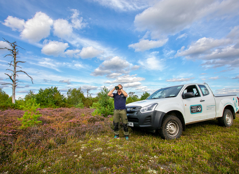 Surrey Wildlife Trust colleague looking through binoculars while standing by a Surrey Wildlife Trust branded van.